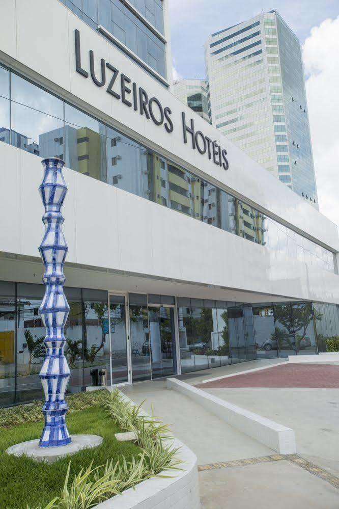 Hotel Luzeiros Recife Exterior foto The photo shows a modern hotel building with large glass windows and a sleek, white facade. In front of the hotel, there is a tall, decorative sculpture that features a unique, twisting shape with a blue and white color scheme. The hotel name is prom